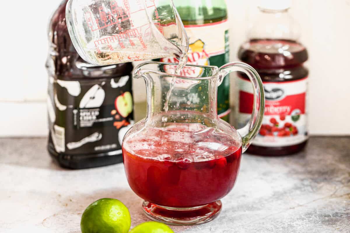 Ginger ale being poured into a pitcher of homemade cranberry punch.
