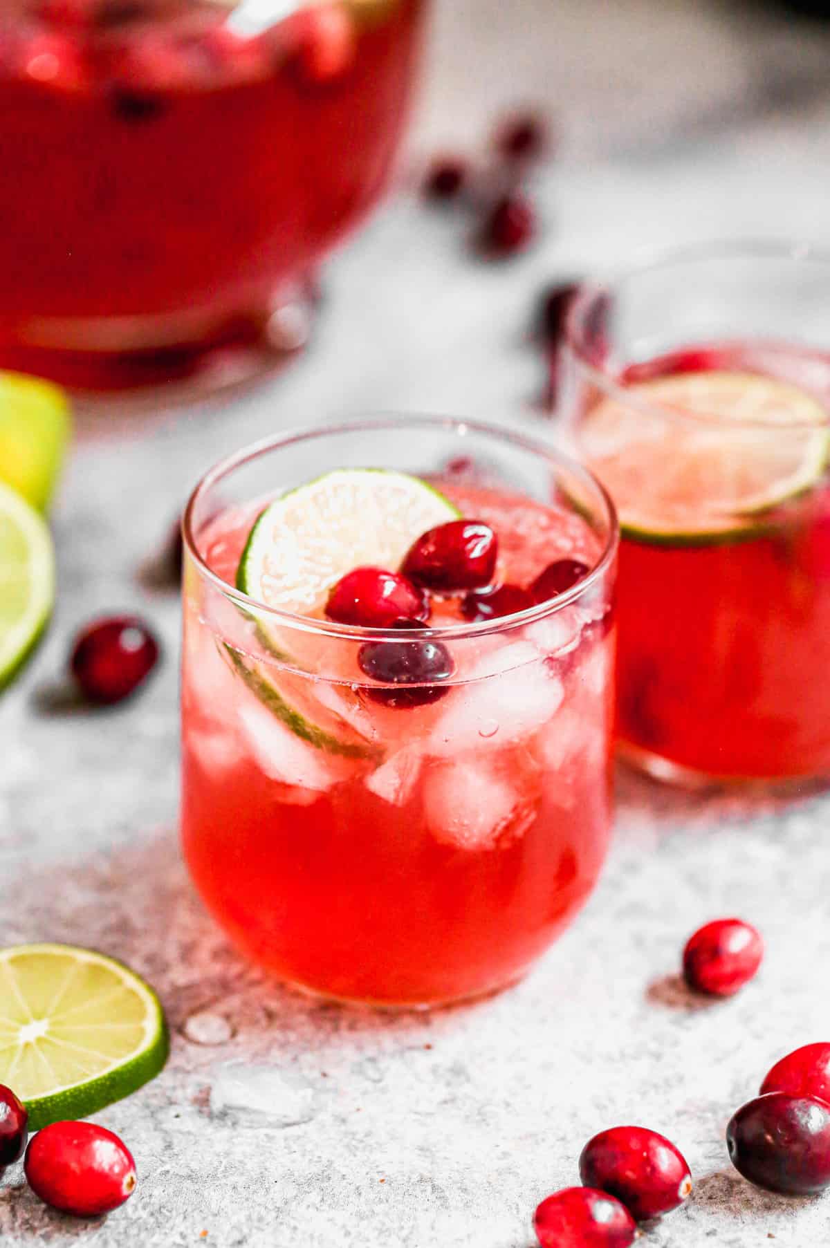 A small glass filled with an easy Christmas Punch recipe, topped with fresh cranberries and a slice of lime.