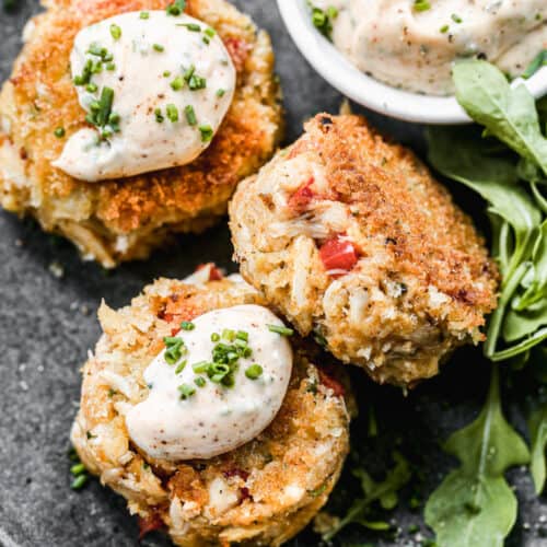 Three easy homemade Crab Cakes on a plate, two of them topped with homemade tarter sauce and garnished with chives.