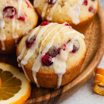 A close up image of homemade Cranberry Orange Muffins on a platter, drizzled with a homemade orange glaze.