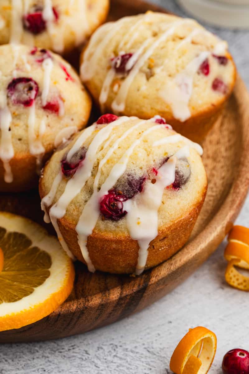 A close up image of homemade Cranberry Orange Muffins on a platter, drizzled with a homemade orange glaze.