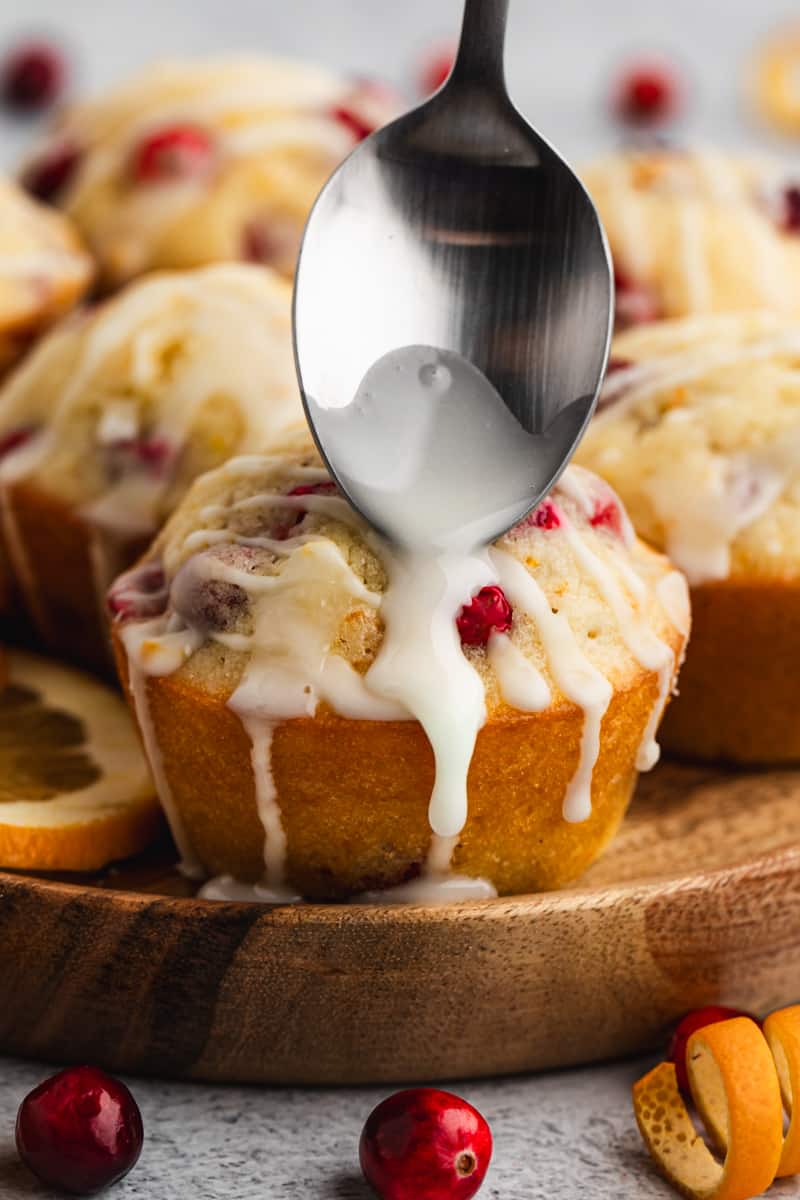 A close up image of orange glaze being drizzled on top of a Cranberry Orange Muffin.