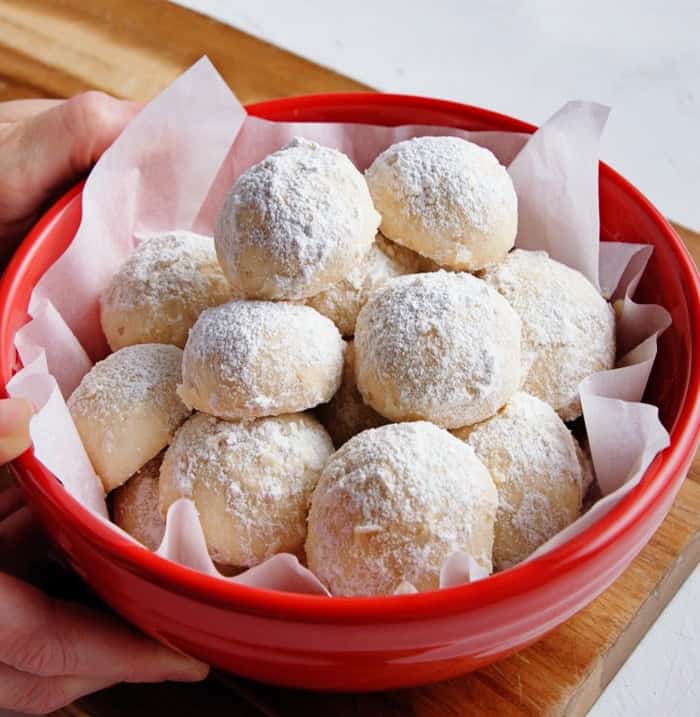 A red bowl filled with easy Snowball Cookies.