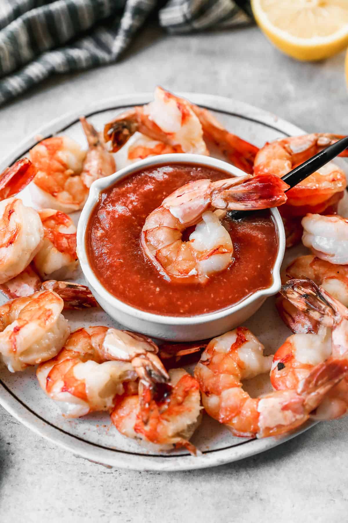 A platter of shrimp and a bowl in the middle for an easy Shrimp Cocktail sauce and one shrimp on top of the sauce.