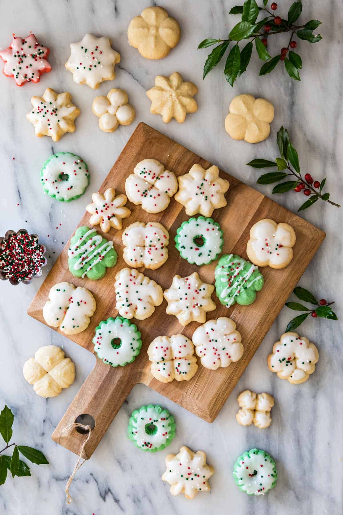 Hoemmade Spritz cookies on a cutting board with a white glaze and holiday sprinkles.