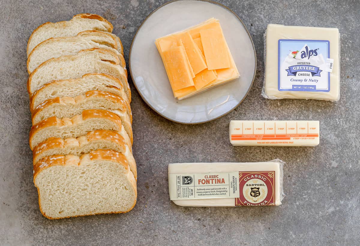 All of the ingredients to make air fryer grilled cheese sandwiches: bread, cheddar cheese, fontina cheese, gruyere, and butter.