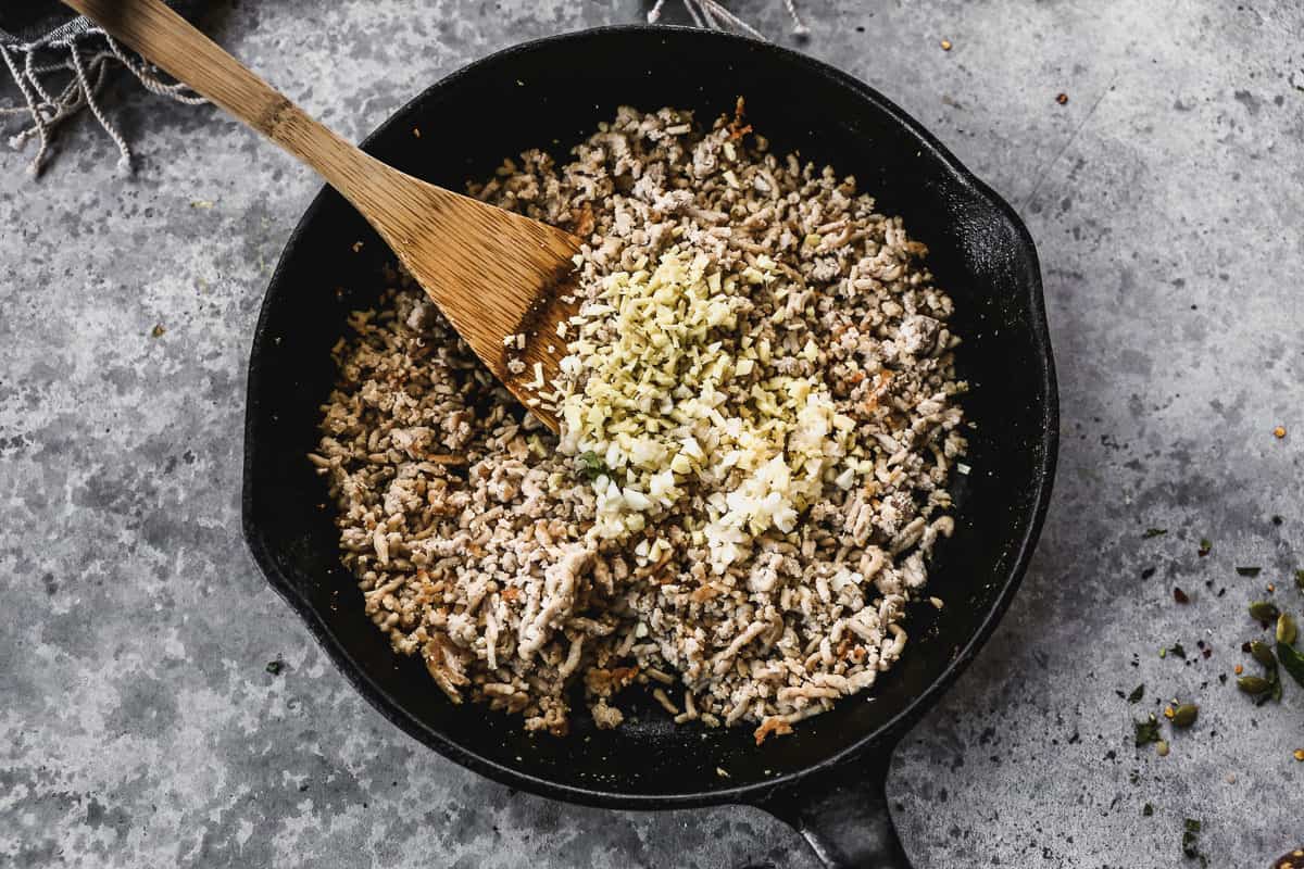 A cast iron skillet with cooked ground pork and garlic.