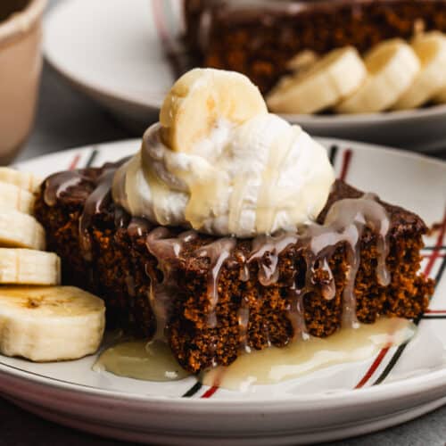 A piece of moist Gingerbread Cake, topped with whipped cream, bananas, and a homemade vanilla cream sauce.