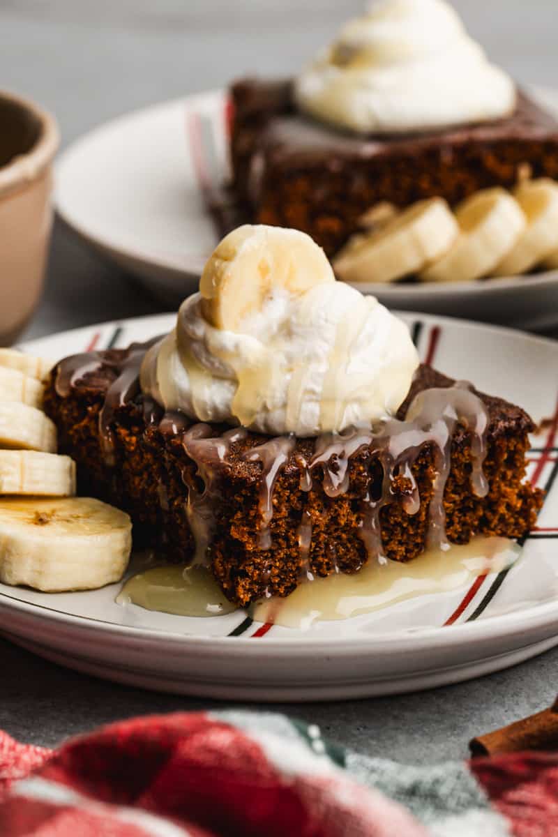 A piece of moist Gingerbread Cake, topped with whipped cream, bananas, and a homemade vanilla cream sauce.