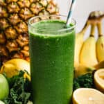 An easy Green Smoothie recipe in a glass with fruit in the background, ready to be enjoyed.