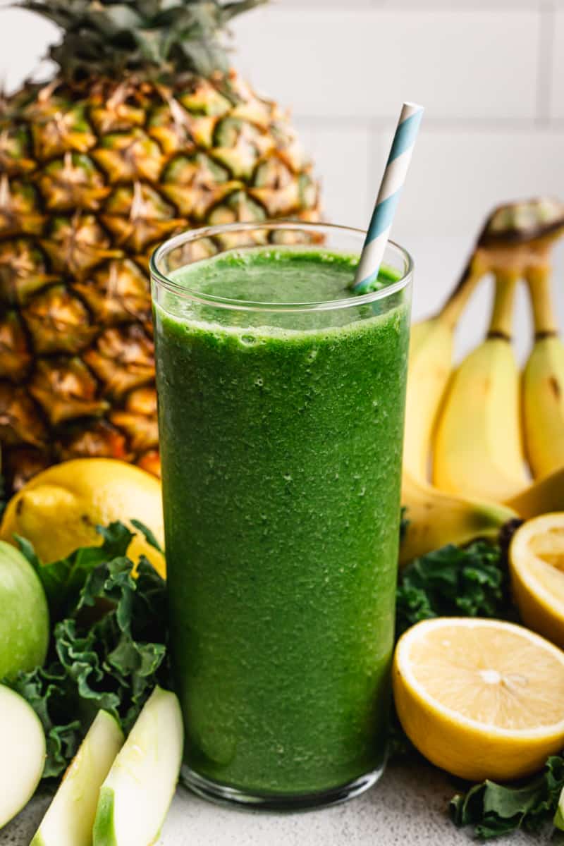 An easy Green Smoothie recipe in a glass with fruit in the background, ready to be enjoyed. 