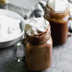 A homemade hot cocoa recipe in glass mugs, topped with fresh whipped cream.