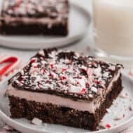 A square of homemade Peppermint Brownies on a white plate, topped with crushed candy canes.