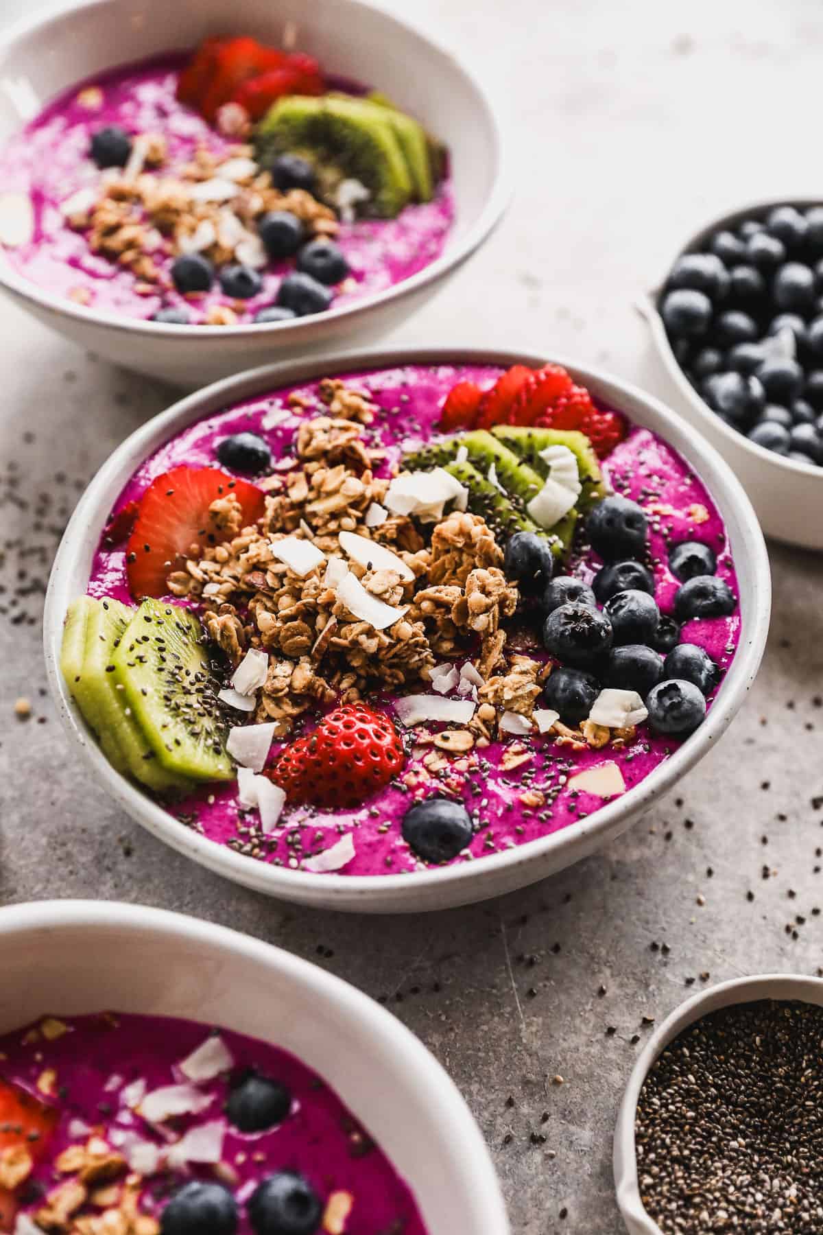 A pitaya smoothie bowl topped with homemade granola, sliced kiwi, strawberries, chia seeds, blueberries, and coconut flakes, ready to enjoy.