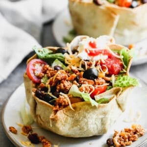 An easy Taco Salad recipe piled high in a crunchy tortilla bowl and topped with vegetables, sour cream, and salsa.