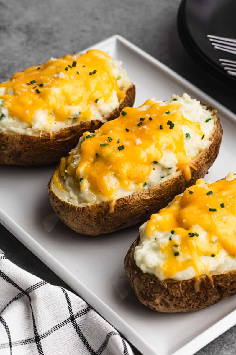 Three Twice Baked potatoes topped with melted cheddar cheese and chives, on a white plate.