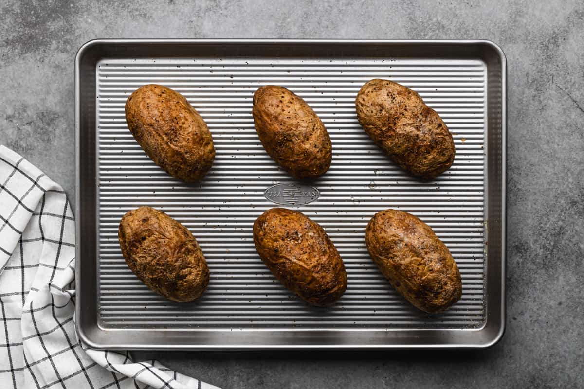 Six baked potatoes on a baking sheet, fresh out of the oven.