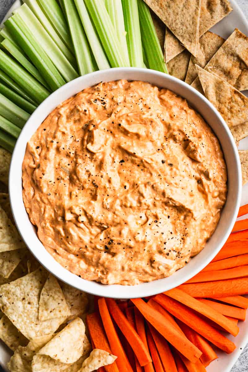 An easy Buffalo Chicken recipe in a white bowl surrounded by chips, celery, and carrots.