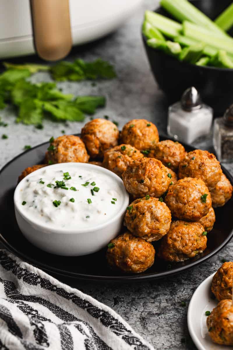Air Fryer Buffalo Chicken Meatballs stacked on a plate with a bowl of homemade bleu cheese dipping sauce.