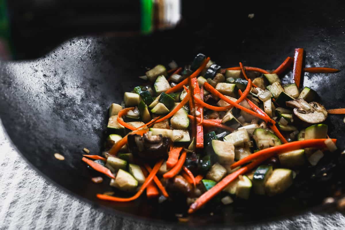 Chopped zucchini, carrot, and mushrooms being sautéed in a wok.