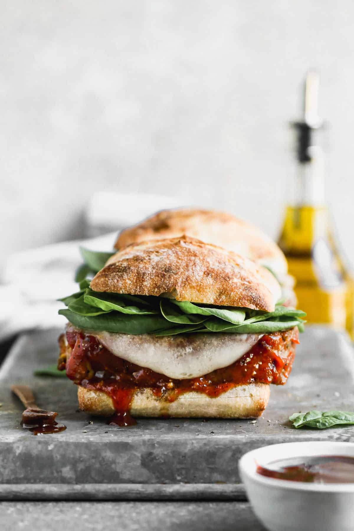 A cold meatloaf sandwich topped with sauce, melted cheese, and spinach on a toasty ciabatta roll.