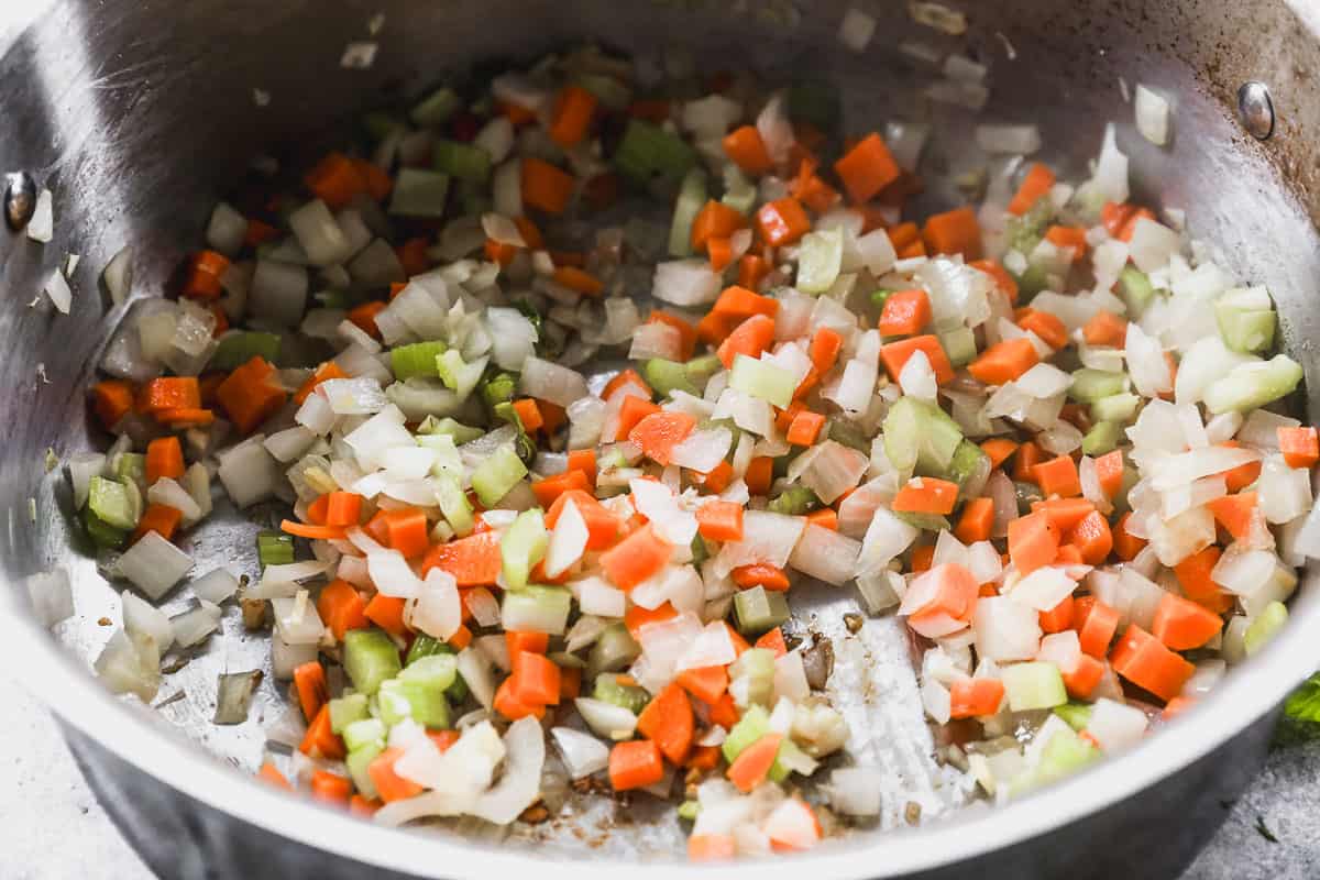 Diced carrots, celery, garlic, and ginger being sautéed in a large pot.
