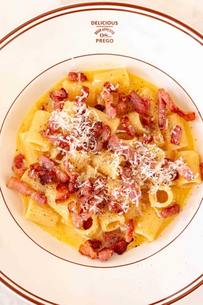 A plate of authentic Pasta Carbonara topped with crispy pancetta, pecorino cheese, and cracked black pepper.