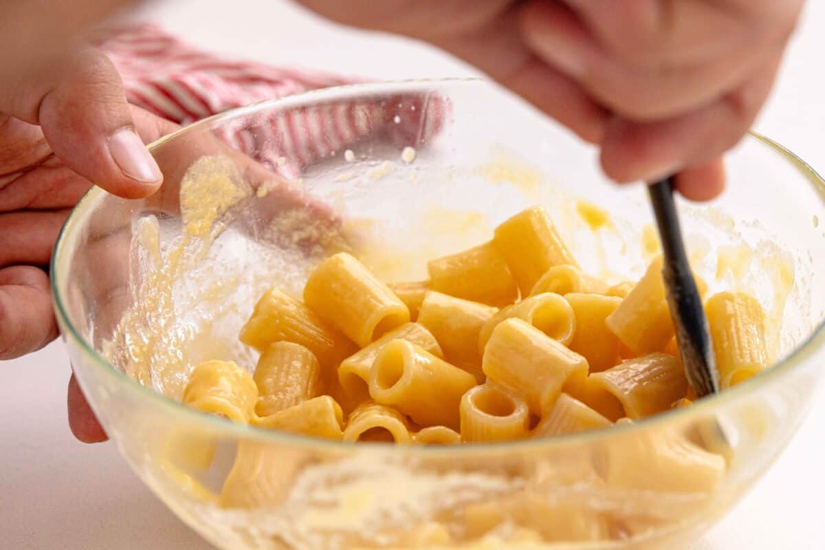 A creamy carbonara sauce coating a bowl of cooked rigatoni pasta to show how to make Pasta Carbonara. 