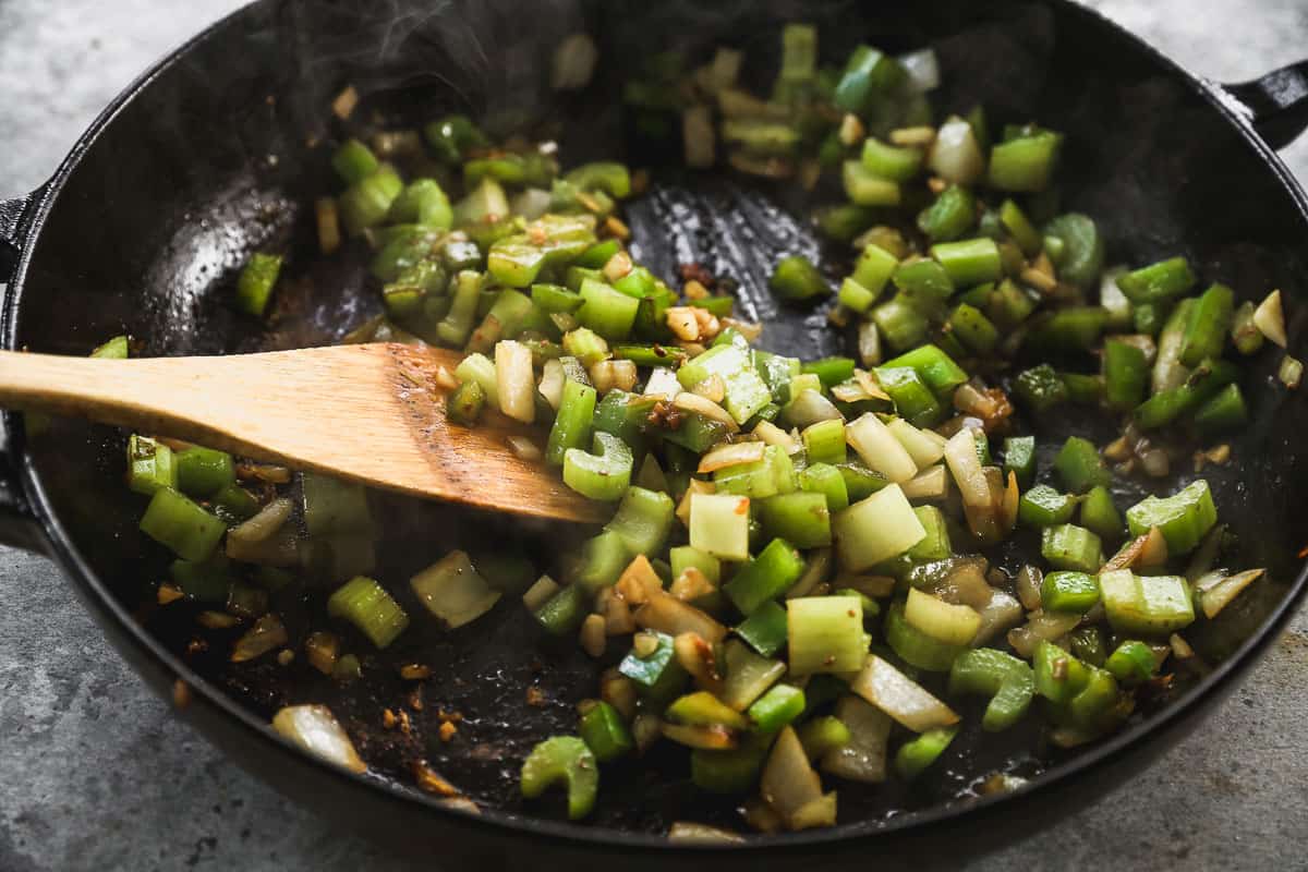 Chopped bell pepper, celery, and garlic being sautéed in a cast iron pan.