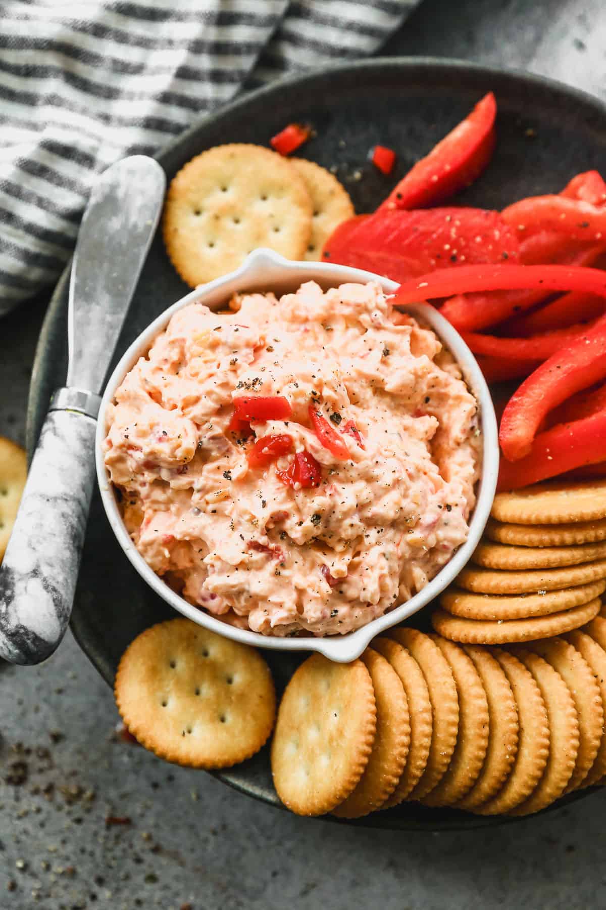 The BEST Pimento Cheese Dip on a plate next to sliced red peppers and crackers for dipping.