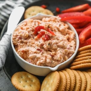 The BEST Pimento Cheese Dip on a plate next to sliced red peppers and crackers for dipping.