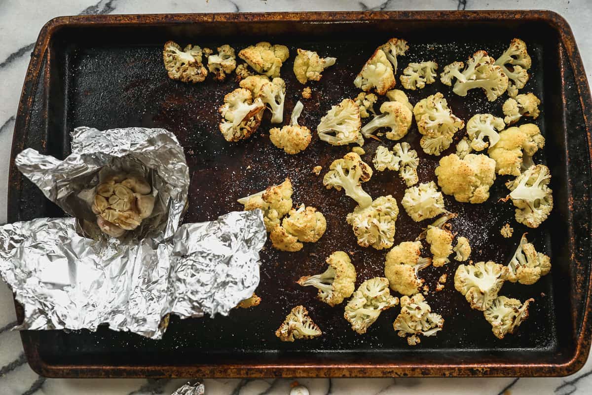 Roasted cauliflower and a bulb of garlic on a baking sheet to make easy Cauliflower Soup.