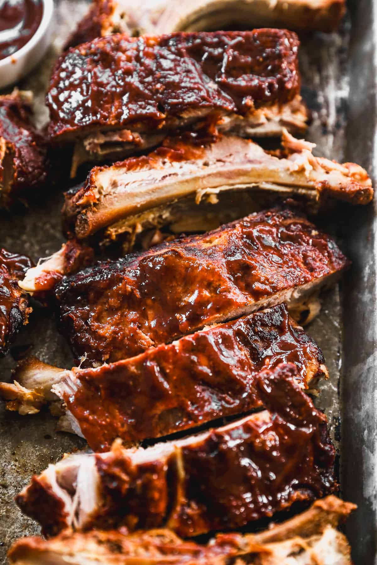 A close up image of the Best Slow Cooker Ribs on a baking sheet, smothered in homemade BBQ sauce.