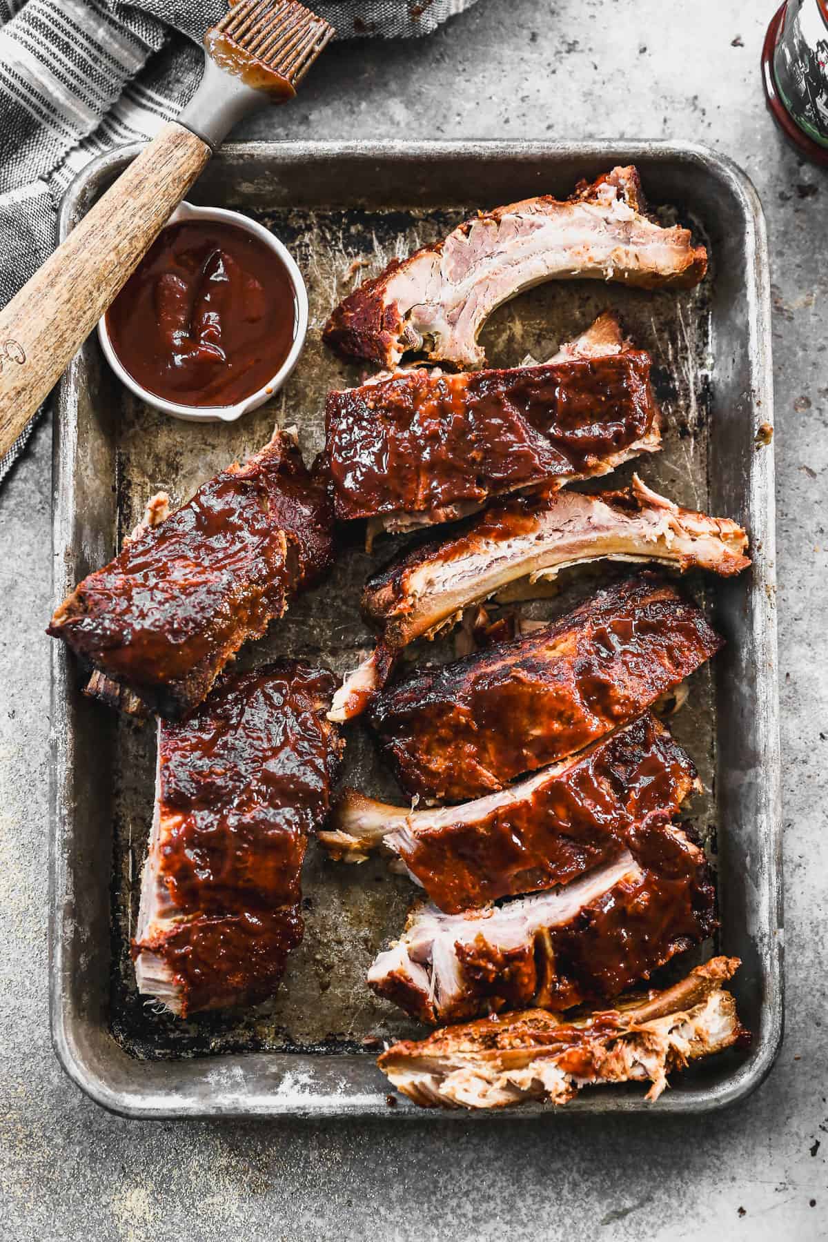 A baking sheet with easy crockpot ribs cut into pieces and served with a side of bbq sauce.