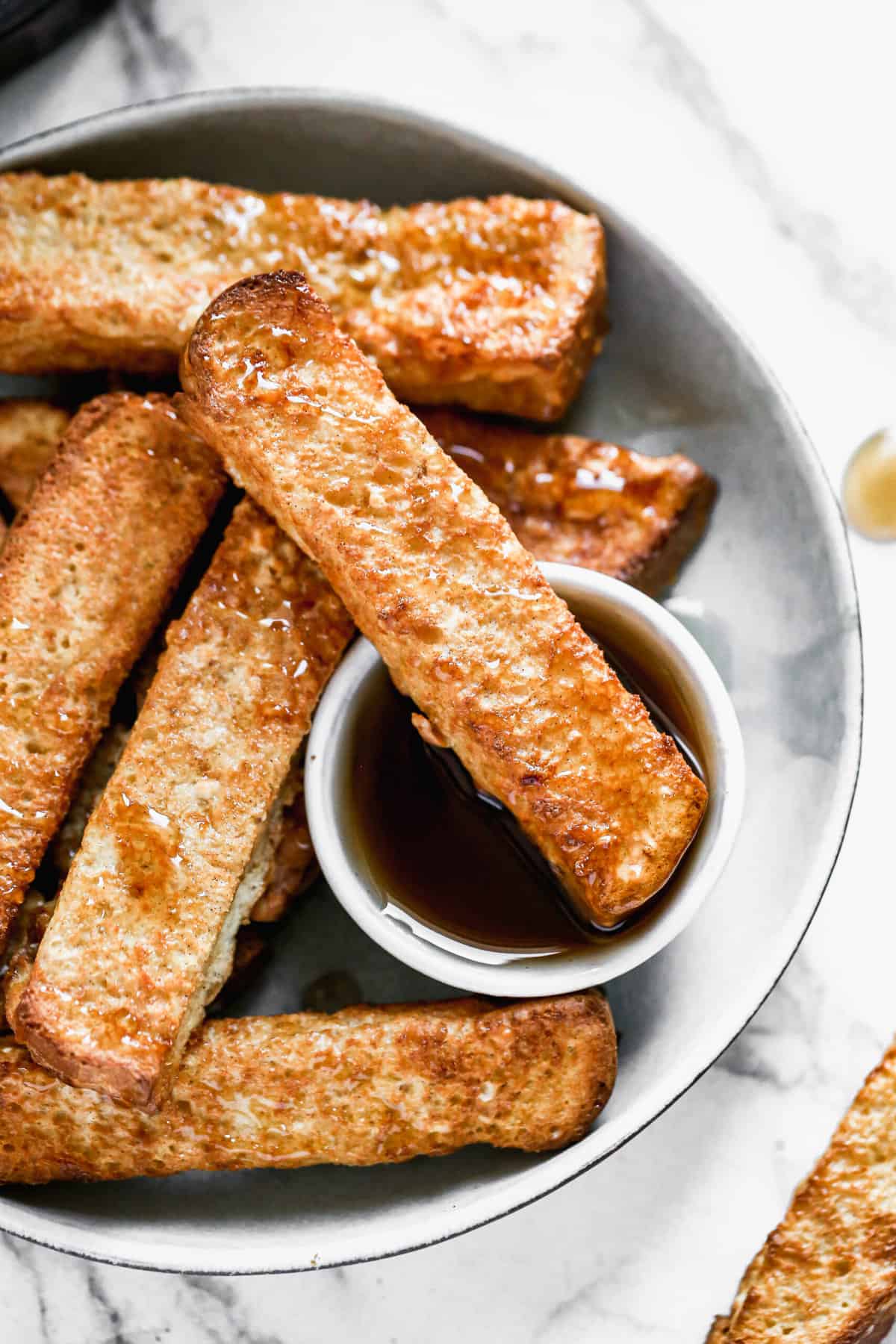 Air Fryer French Toast served on a plate, with one being dipped in a little bowl of syrup.