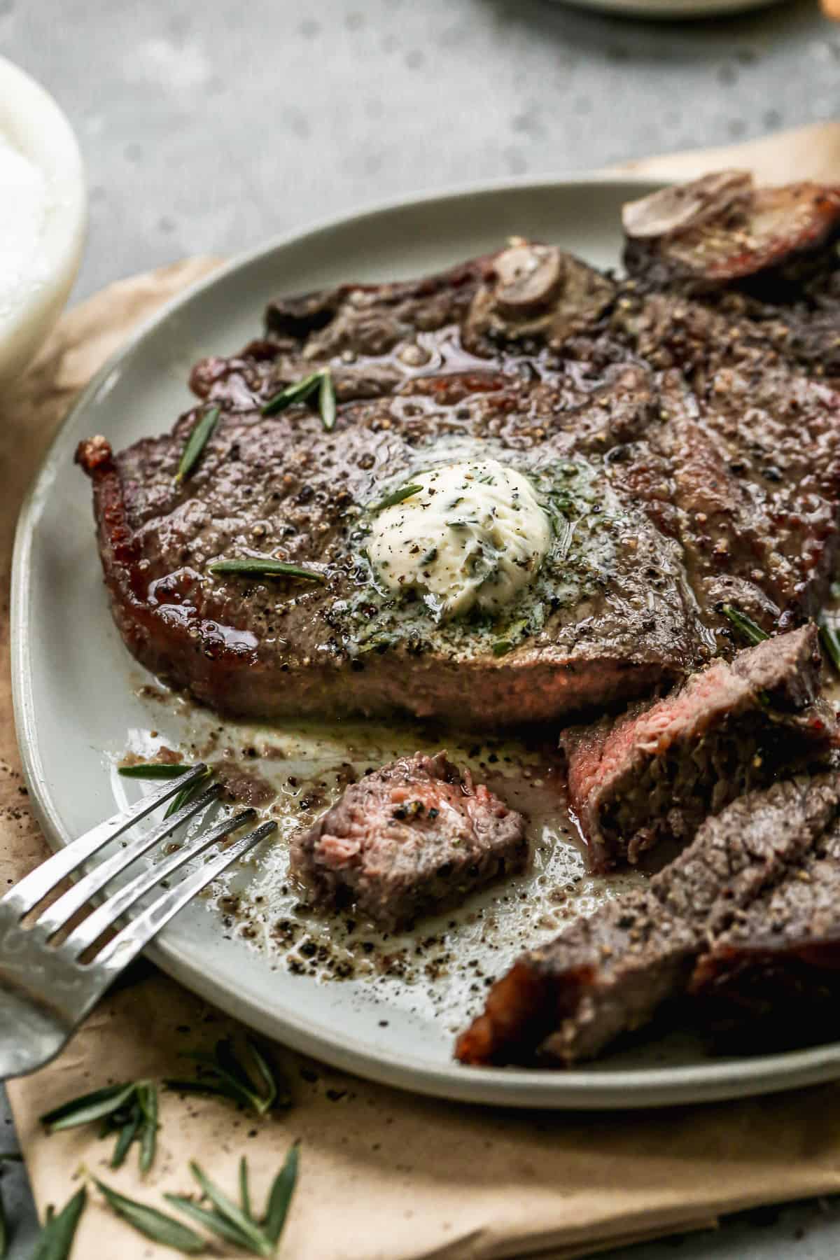 The best air fryer steak topped with homemade garlic butter with a piece cut to show the juicy interior. 