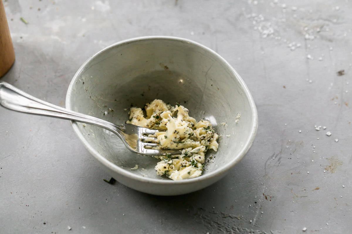 A fork combining butter, rosemary, and garlic to make a simple garlic butter.