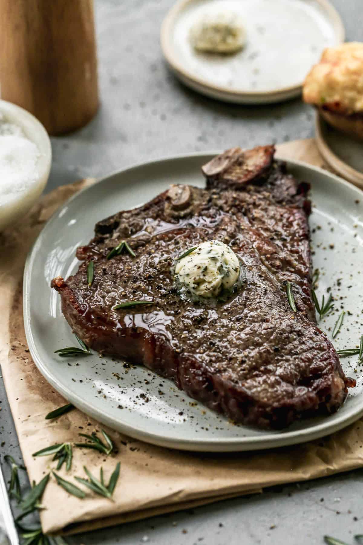 An easy air fryer steak on a plate, topped with a scoop of fresh herb butter. 