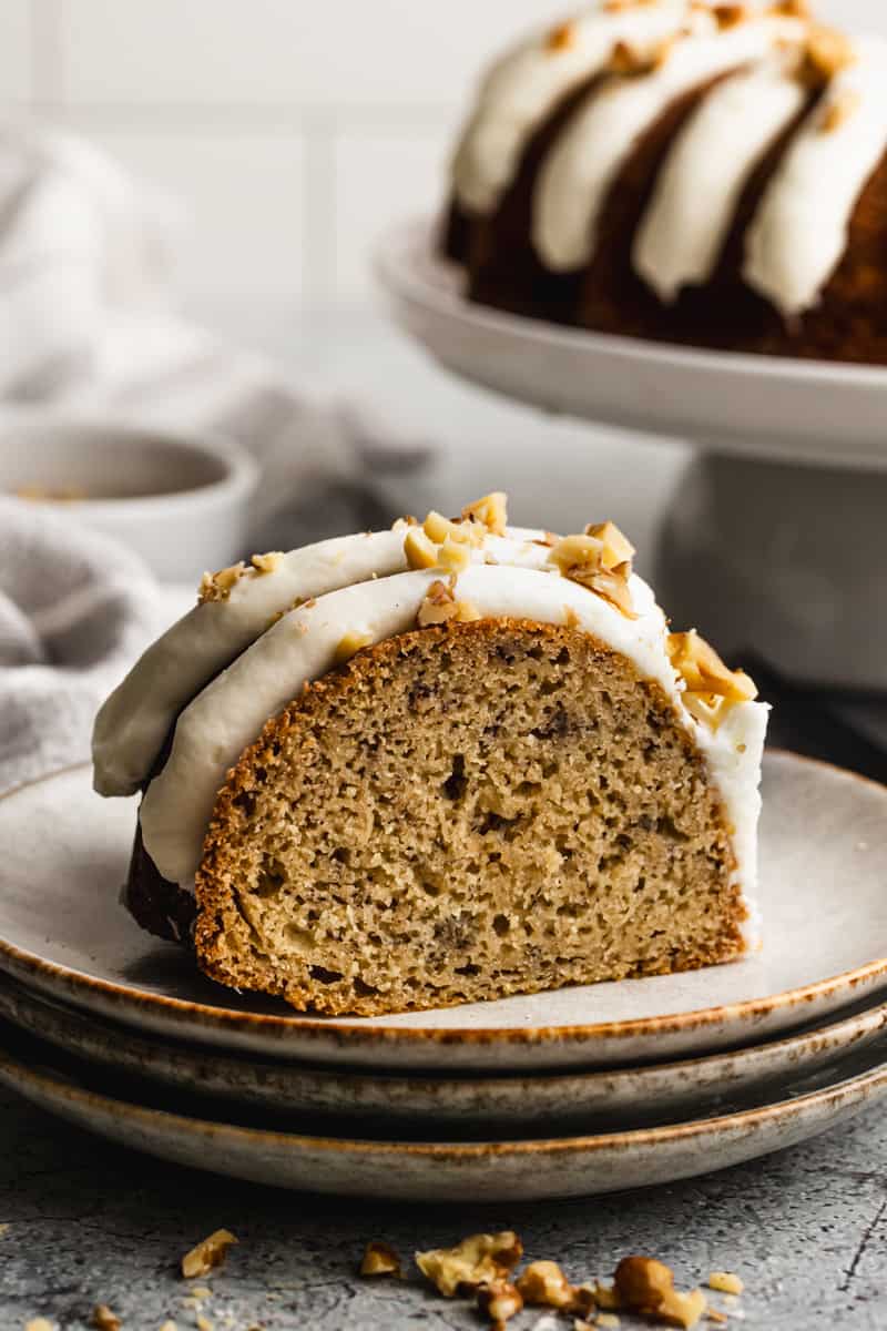 A slice of a banana cake recipe made in a bundt pan and frosted with cream cheese frosting and chopped walnuts.