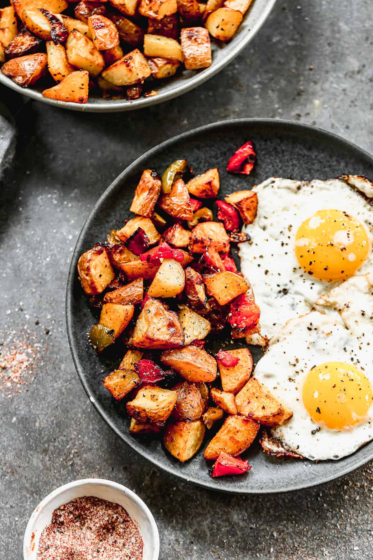 Easy breakfast potatoes roasted until crispy on a plate next to two fried eggs, sunny side up. 