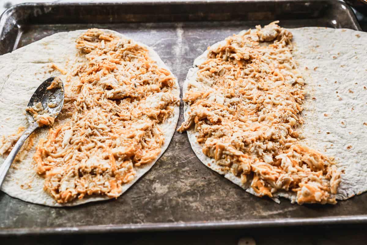 A chicken mixture being spread on half of a tortilla for the best Chicken Quesadilla recipe.