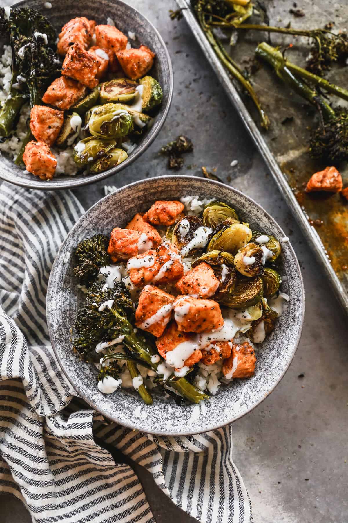 A Hot Honey Salmon Bowl with roasted broccolini and brussels sprouts on a bed or rice and drizzled with hot honey and ranch. 
