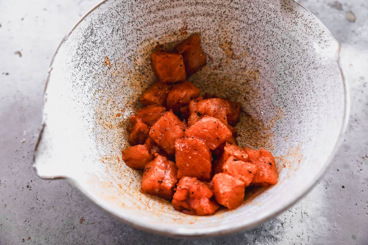 Pieces of a salmon fillet cut into chunks and in a bowl, tossed with olive oil, salt, pepper, garlic powder, and smoked paprika. 