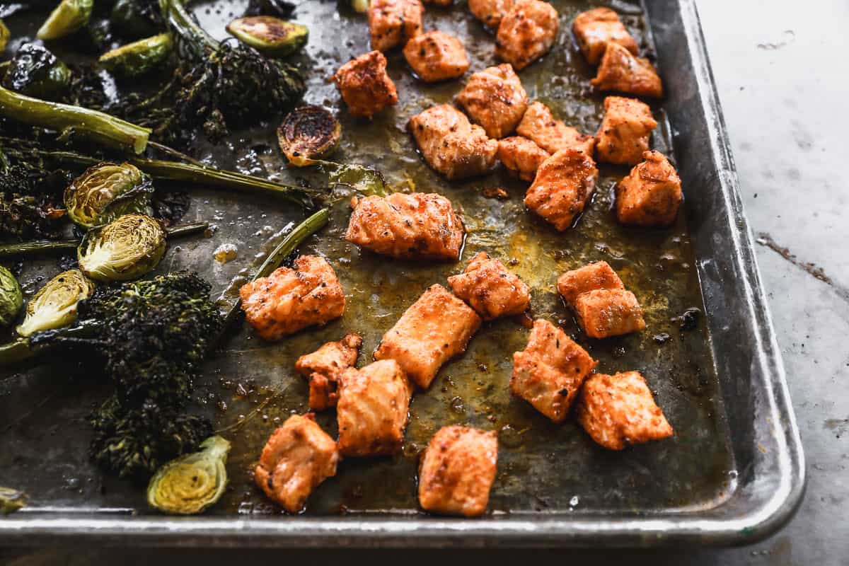 A sheet pan with hot honey salmon bites and roasted broccolini and brussels sprouts.