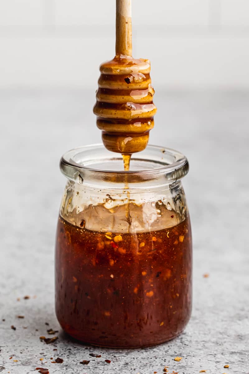 An image showing a honey dipper being lifted out of a jar of a homemade hot honey sauce recipe. 
