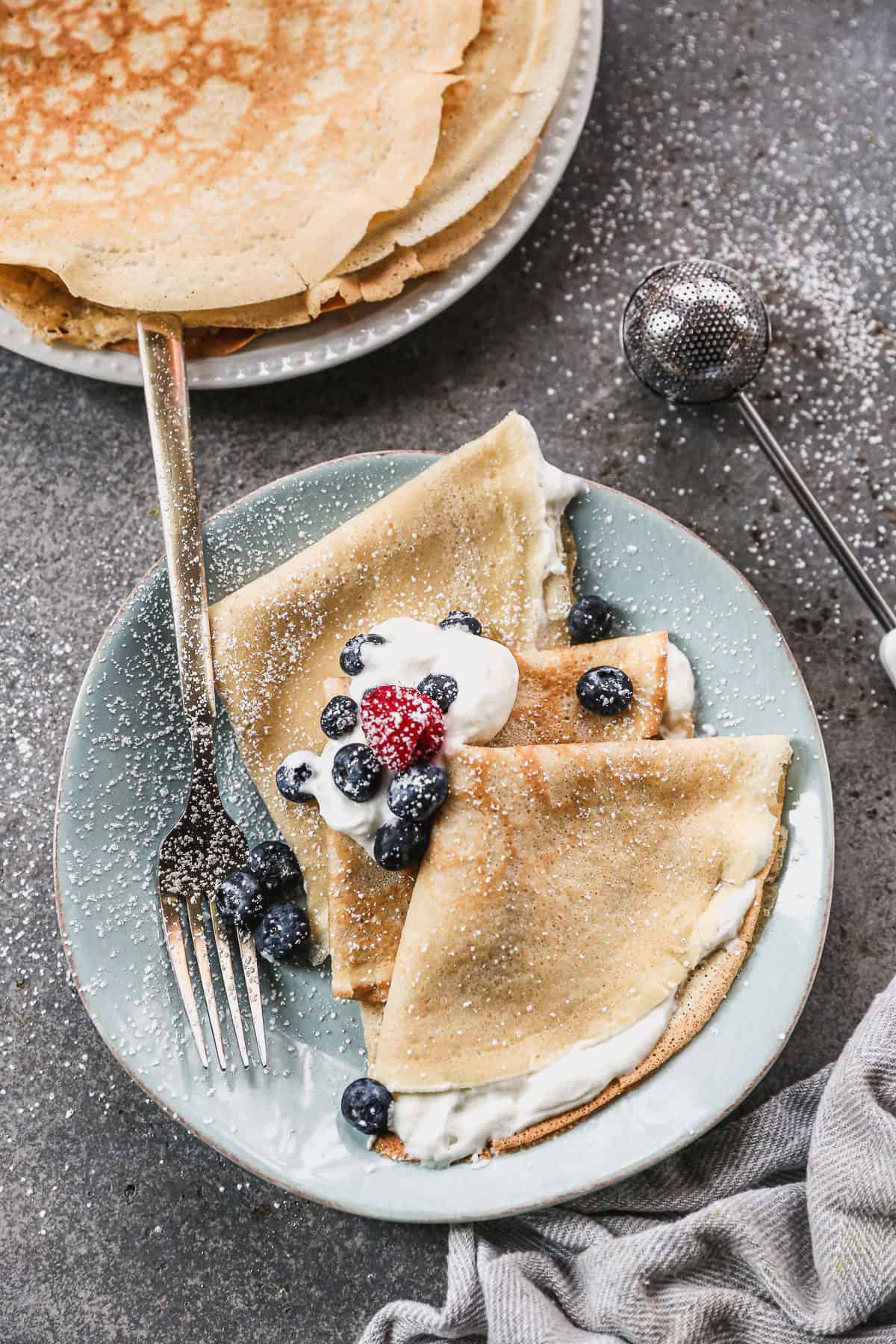 A plate with three French crepes on it, folded into a triangle and served with whipped cream and fresh berries.