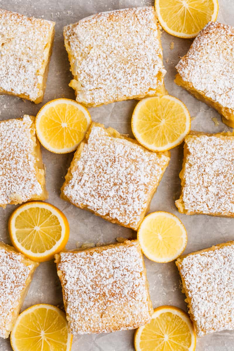 The best Lemon Bar recipe cut into squares and placed on a piece of parchment with sliced lemons.