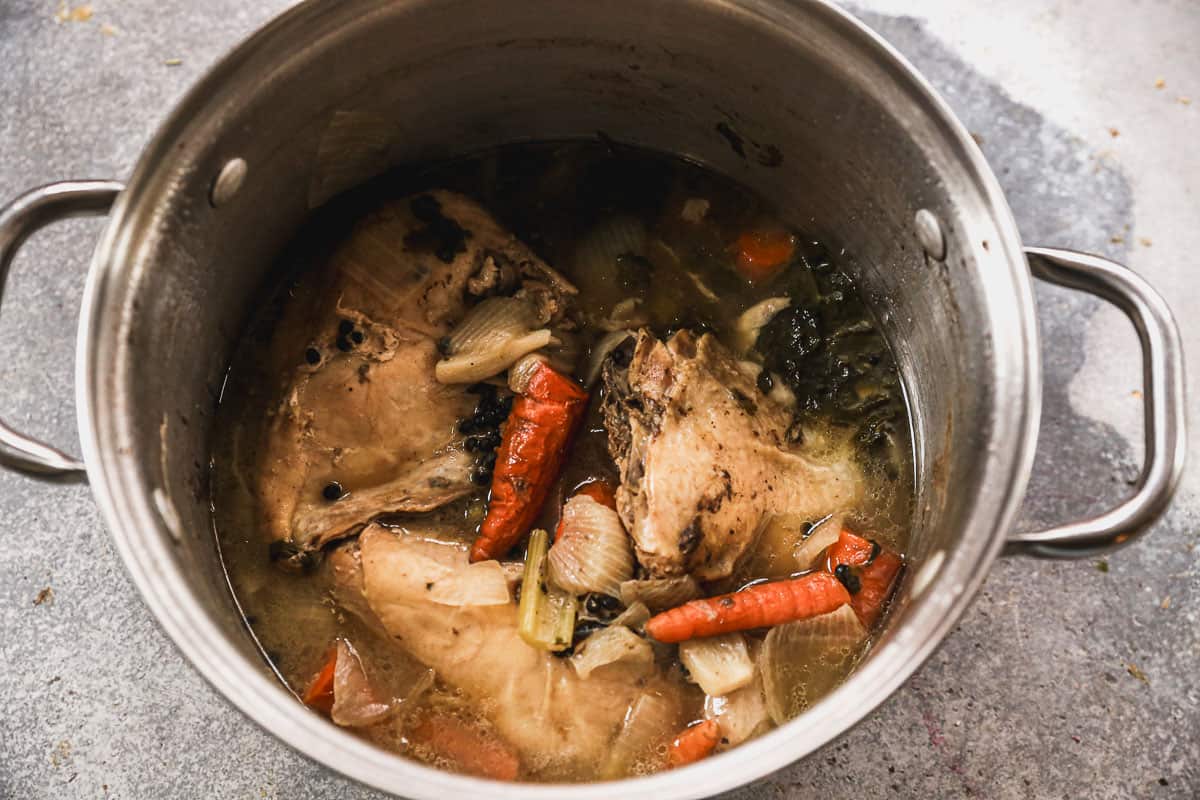 A pot with chicken and veggies being cooked with vegetables to create a soup broth.