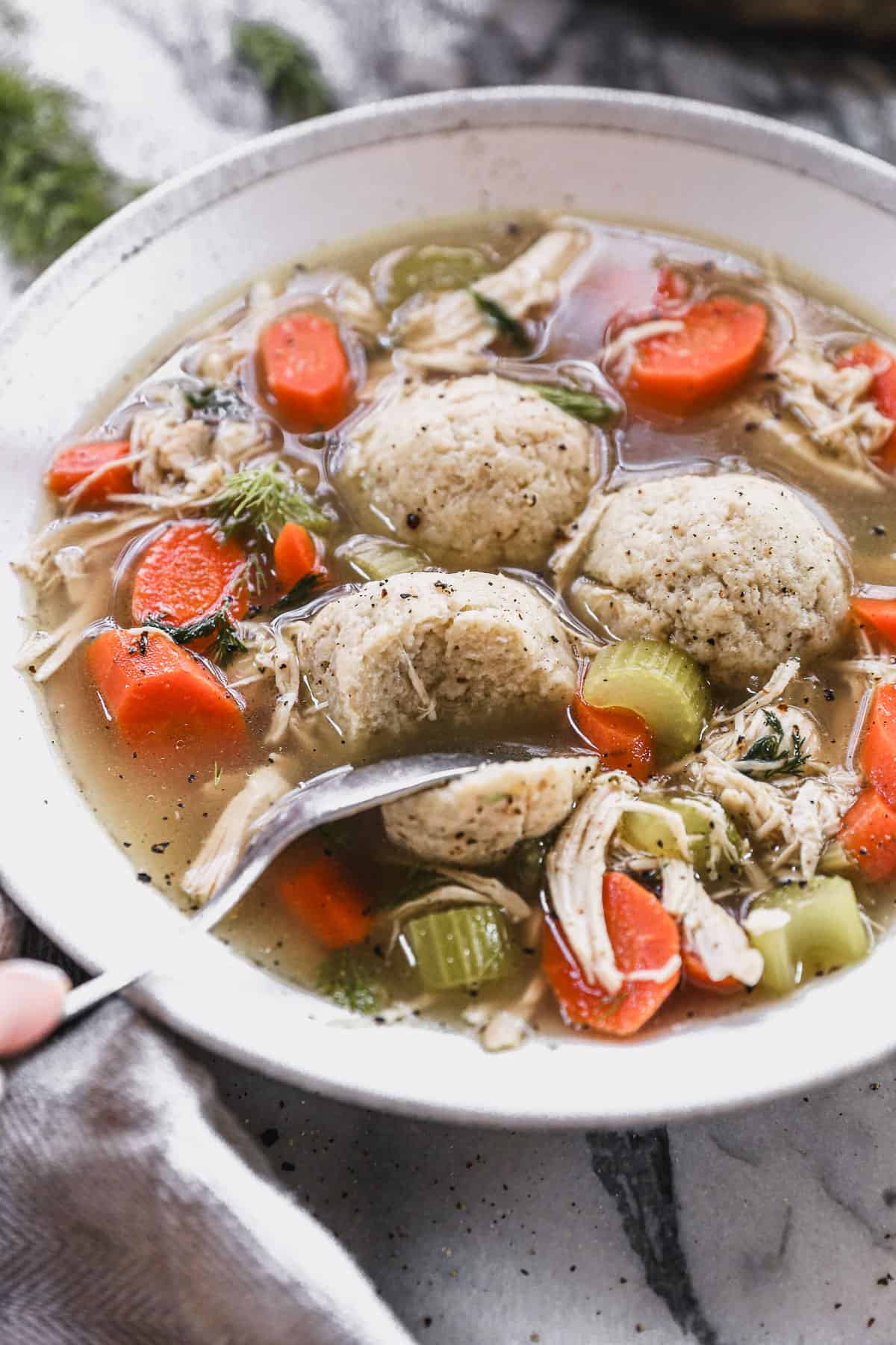 The best Matzo Ball Soup recipe served in a white bowl with a spoon cutting into a homemade matzo ball.