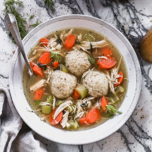 The best Matzo Ball Soup recipe served in a bowl with a flavorful broth with carrots, celery, and herbs and three matzo balls.